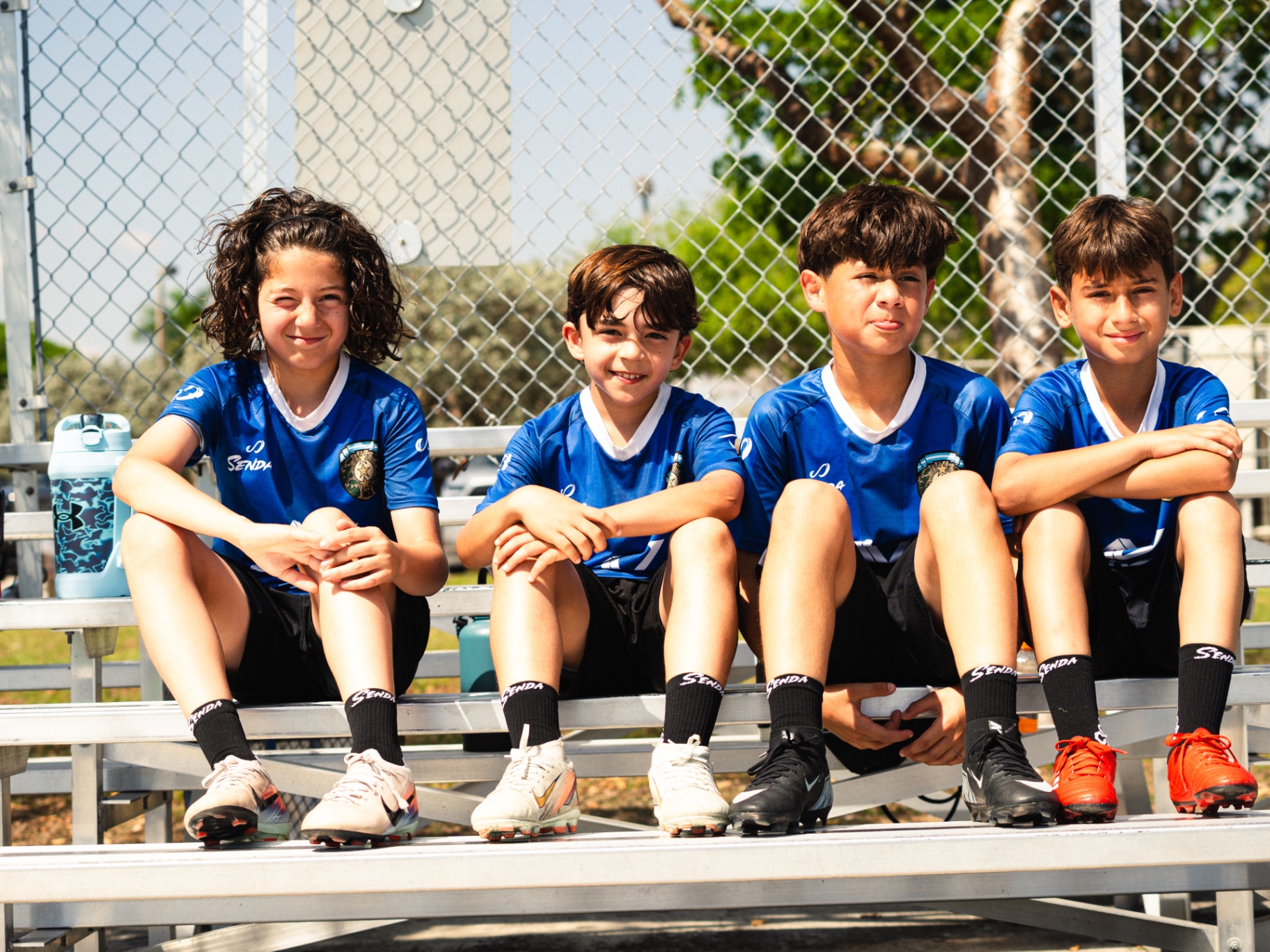 Four young camp players sitting on the bleachers in blue kits